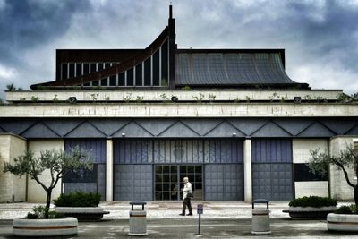 Man walking on city street against cloudy sky