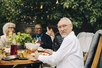 Portrait of smiling elderly man sitting with friends enjoying dinner at dining table