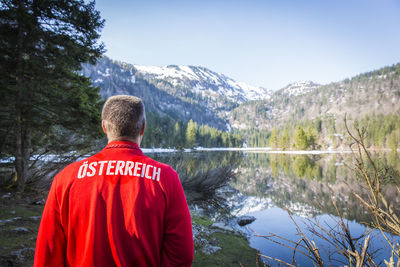 Rear view of person standing by lake against mountain