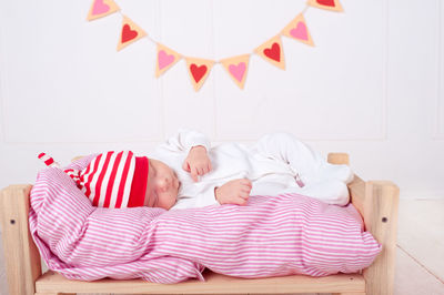 Cute baby wear pajamas and hat sleeping in small bed over white background with heart decorations