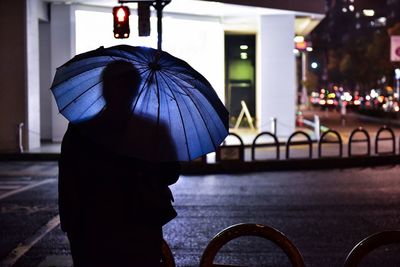 Rear view of woman standing on wet street in rainy season