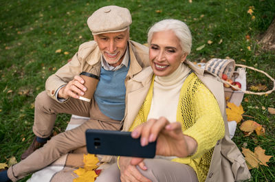 Smiling woman doing selfie while sitting with husband at park