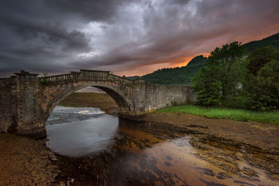 Arch bridge over river against sky during sunset