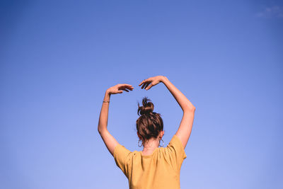 Rear view of woman dancing against clear blue sky