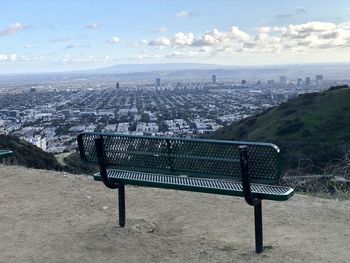 Bench in city against sky