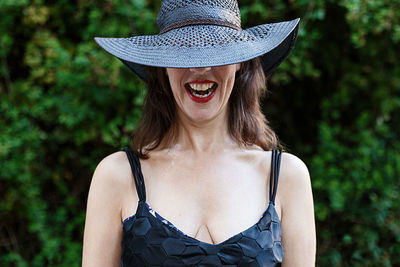 Smiling woman wearing hat standing against plants