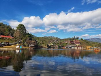 Scenic view of lake by trees and buildings against sky