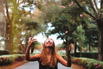 Young woman throwing petal mid-air while standing at park