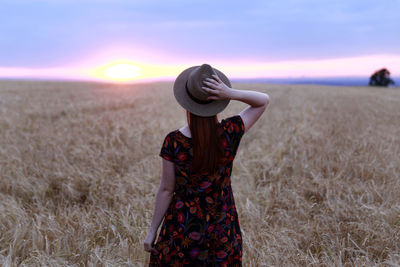 Rear view of woman standing on field during sunset