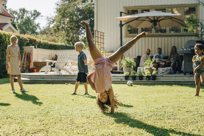 Girl doing cartwheel while playing with friends in backyard on sunny day