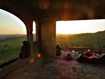 People sitting on landscape against sky during sunset