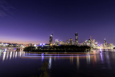 Illuminated buildings by river against sky at night