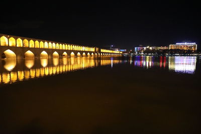 Illuminated bridge over river against sky at night