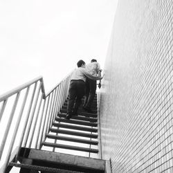 Low angle view of men photographing on steps against sky