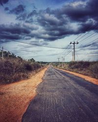 Road by electricity pylon against sky