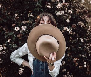 Young woman holding hat while standing against plants