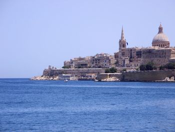 Buildings by sea against clear sky