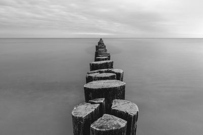 Wooden posts on pier over sea against sky