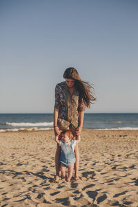 Woman standing with baby at beach against clear sky