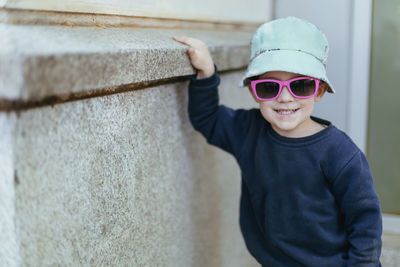 Portrait of young man wearing sunglasses standing against wall