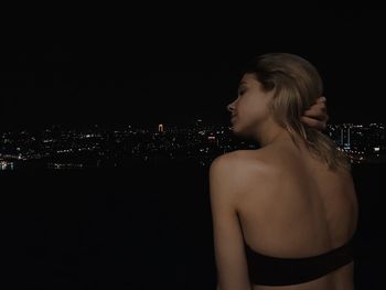 Rear view of shirtless woman in illuminated city at night