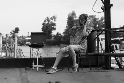 Woman listening music while sitting on chair against clear sky