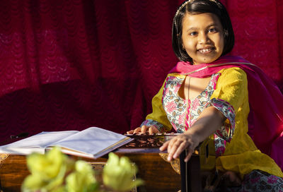 An indian cute girl child looking at camera and playing harmonium in ethnic dress