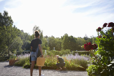 Rear view of female florist carrying basket towards colleague crouching by flower plants