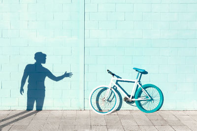 Shadow of unrecognizable man on blue wall near stylish bicycle parked on sidewalk on sunny day