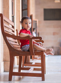 Isolated cute toddler baby boy sitting at wood bench in casual appearance at indoor