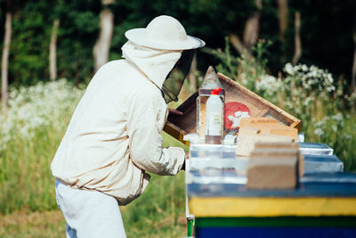 Side view of beekeeper examining beehive on land