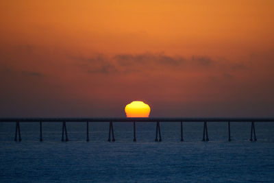 Silhouette wooden post in sea against romantic sky at sunset