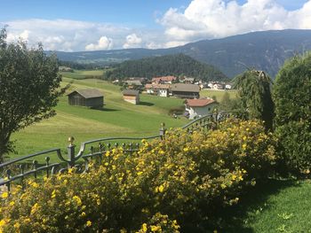 Scenic view of grassy field by houses and mountains against sky