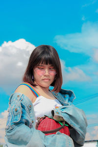 Low angle view of young woman holding purse while standing against blue sky