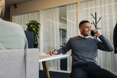 Smiling businessman talking on smart phone sitting at desk in coworking office