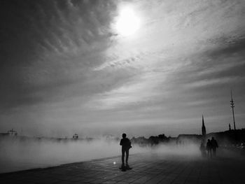 Silhouette man standing on shore against sky