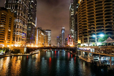 Illuminated bridge over river by buildings in city at night