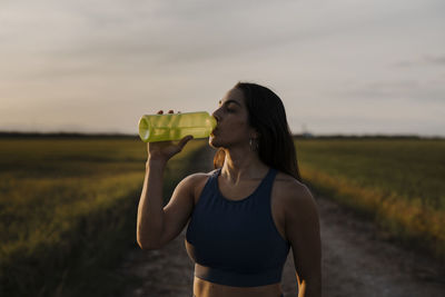 Woman drinking water through bottle against sky