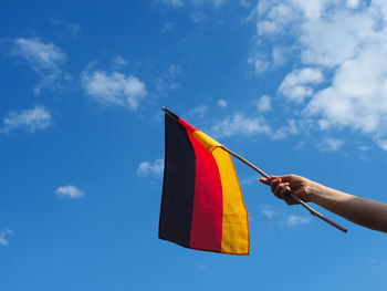 Low angle view of hand holding german flag against sky