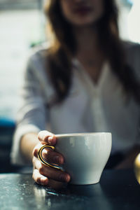 Midsection of woman holding coffee cup at table