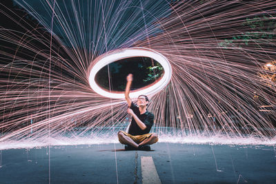 Full length of man with wire wool sitting on road at night