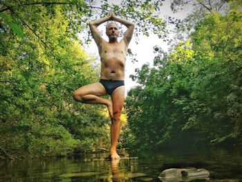 Full length of shirtless man on tree by lake