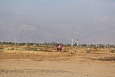 People on field by mountains against sky