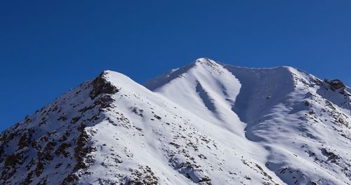 Low angle view of snowcapped mountains against clear blue sky