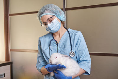 Female doctor wearing protective mask while standing against wall