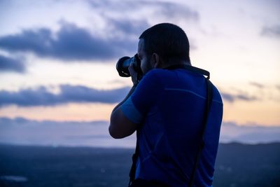 Rear view of photographer photographing against sky during sunset