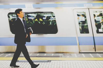 Side view of woman standing by train at railroad station