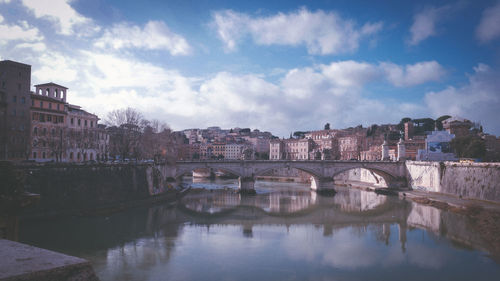 Arch bridge over river against cloudy sky in city