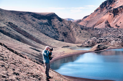 Man standing on mountain by lake against sky