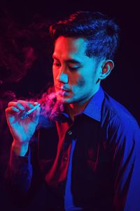 Young man smoking cigarette against black background